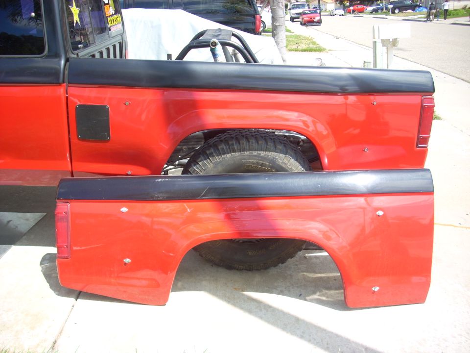 Two red truck bed panels with black trim and visible tire wells. One panel is attached to a vehicle, the other is separate