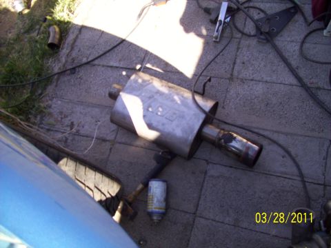 1995 Ford Probe - An exhaust muffler with a visible 'BBK' logo lies on the ground, alongside a tire and a can of spray paint.