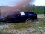 1989 Ford Bronco - Pickup truck stuck in mud with grass and trees in the background.