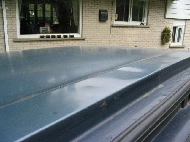 Flat dark hardtop roof of a vehicle in foreground with brick house and windows behind