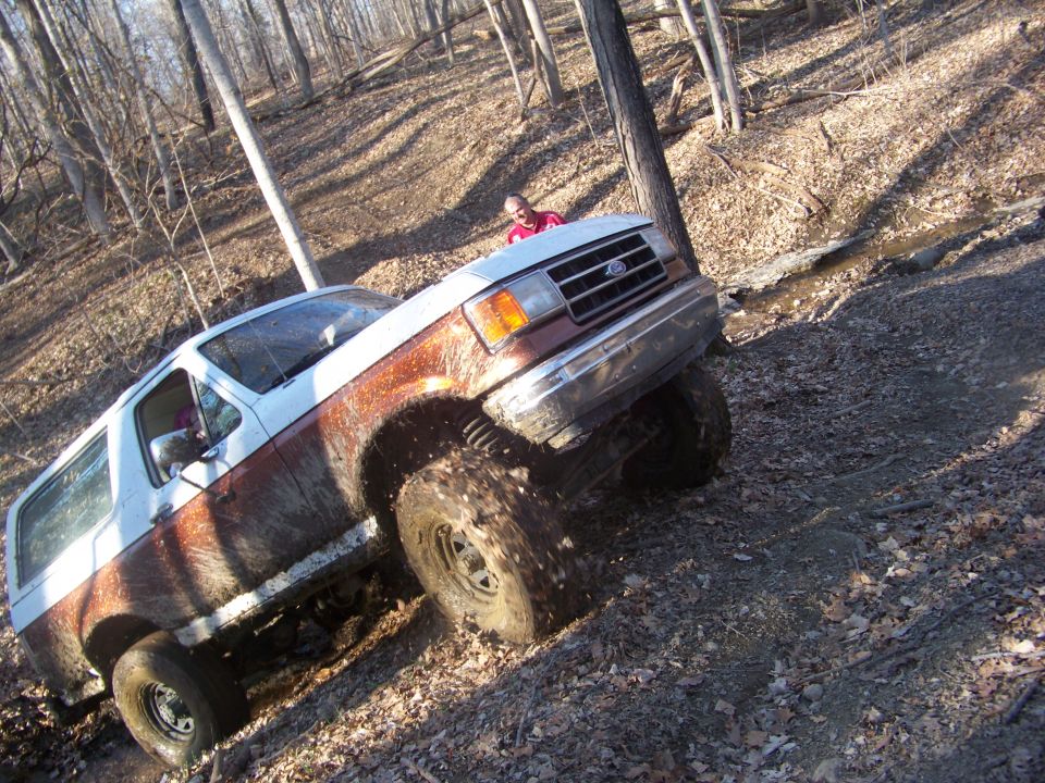 White and brown Ford Bronco climbing a muddy hill in a wooded area