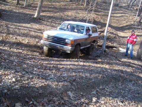 1989 Ford Bronco - A Ford Bronco navigates a challenging muddy trail in a wooded environment.