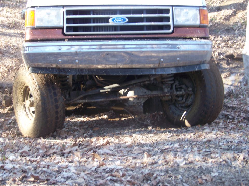 Front of a lifted Ford Bronco with large tires, showing the grille and bumper. The Ford logo is visible on the grille