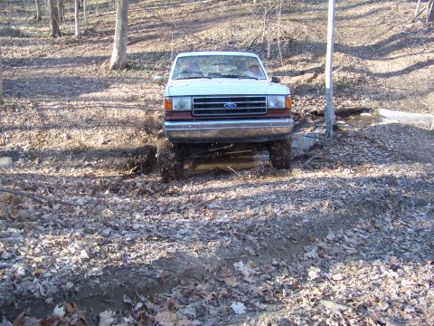 1989 Ford Bronco - This white Ford Bronco is navigating a muddy, wooded area.