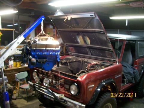 1970 Ford Bronco - A red 1970 Ford Bronco is in a garage with its hood open as an engine is lifted out by a blue engine hoist.