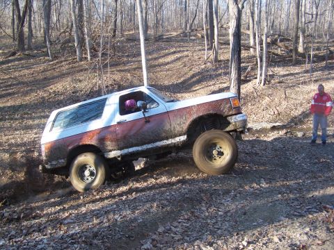 1989 Ford Bronco - Muddy 1989 Ford Bronco navigates rough terrain in a forest setting.