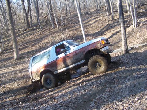 1989 Ford Bronco - This Ford Bronco is navigating a challenging off-road trail covered in mud and fallen leaves.
