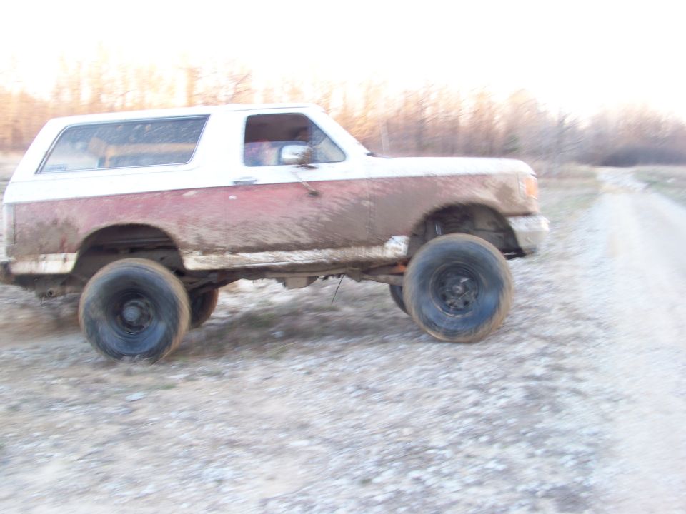 1989 Ford Bronco side view, covered in mud, driving on a dirt road