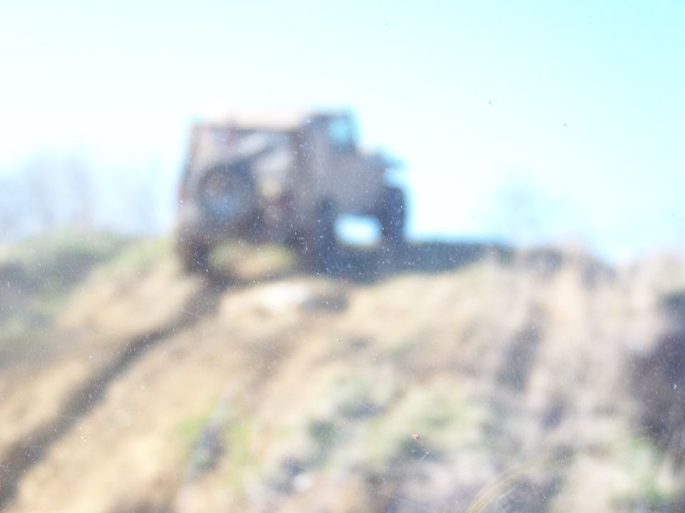 Off-road vehicle driving up a dirt hill, sky is bright blue