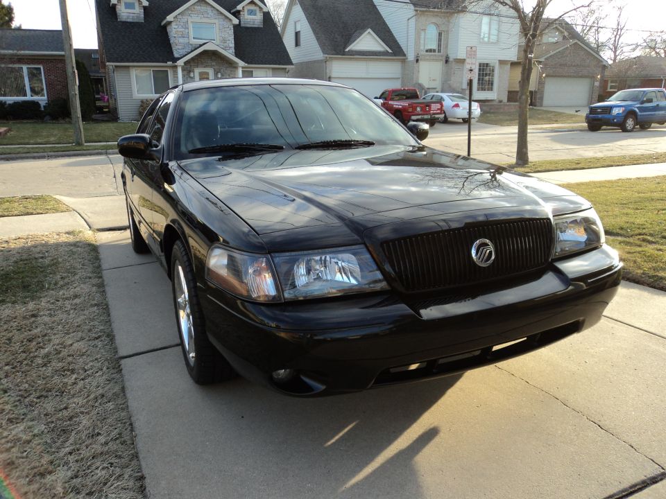 Black Mercury Grand Marquis, front three-quarter view on a suburban driveway with chrome wheels