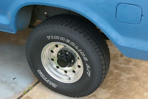 1978 Ford Bronco - Close-up of a blue SUV's rear wheel and fender, showing tire and rim details.
