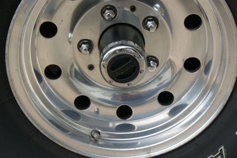 1978 Ford Bronco - Close-up of a chrome wheel with a black hubcap, showing lug nuts and tire tread.