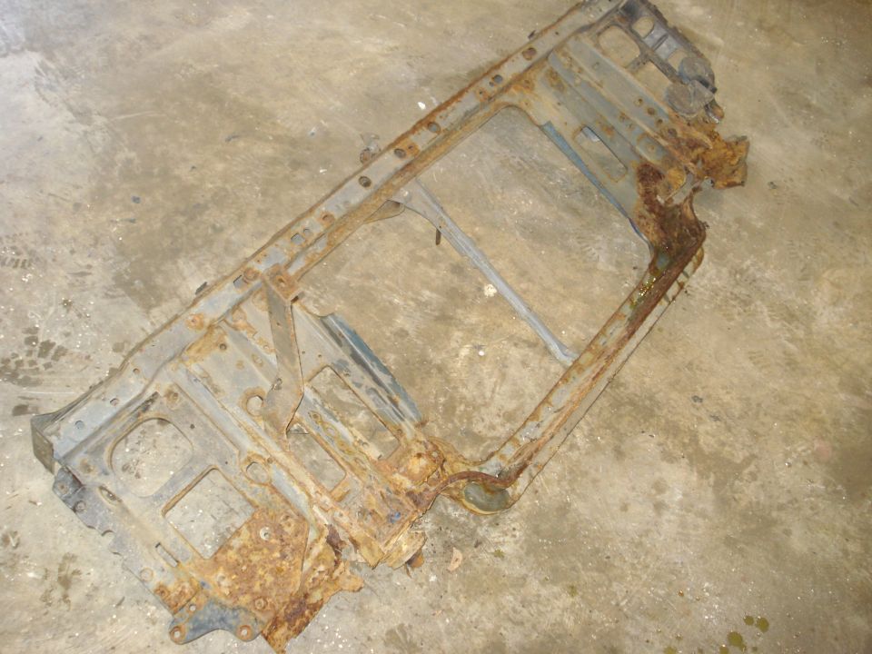 Rusted metal frame with rectangular cutouts and mounting holes, lying on a concrete floor