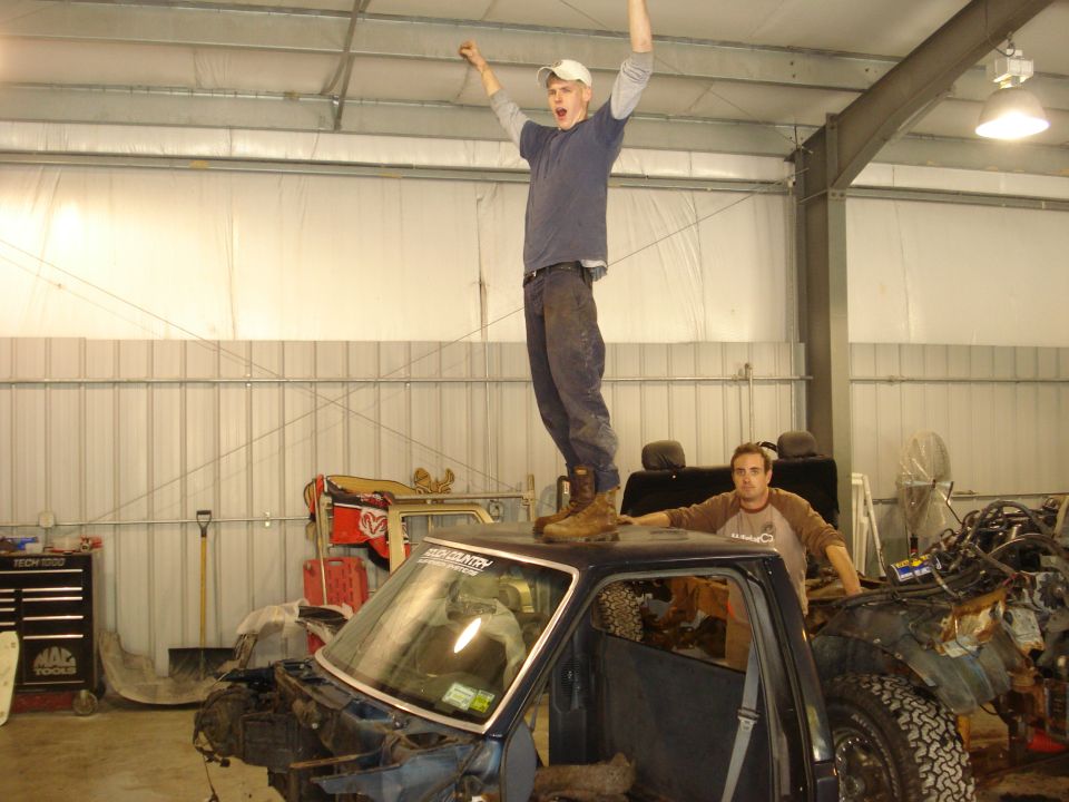 guy on roof of truck, another guy leaning on it, inside garage