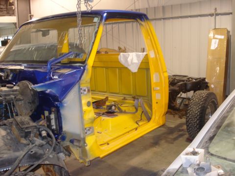 1993 Ford F-150 - A Ford F-150 truck cab, painted blue and yellow, is suspended by chains during a restoration project.