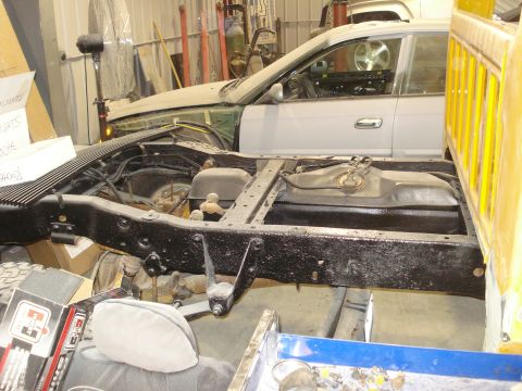 1993 Ford F-150 - The chassis of a truck is shown, with a sedan parked behind it in a workshop.