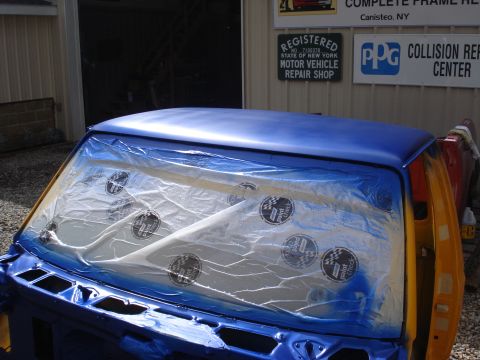 1993 Ford F-150 - A blue truck cab is covered in plastic sheeting, indicating it is being prepped for painting at a repair shop.