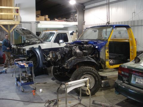1993 Ford F-150 - Two trucks are in a workshop, one a 1993 Ford F-150 in blue and yellow, the other a white truck with its hood open.