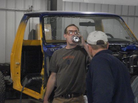 1993 Ford F-150 - Two men are in a garage, one drinking from a can, with a partially restored truck cab in the background.