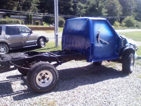 1993 Ford F-150 - A blue pickup truck cab and chassis is visible, undergoing a paint job. Another vehicle is parked in the background.