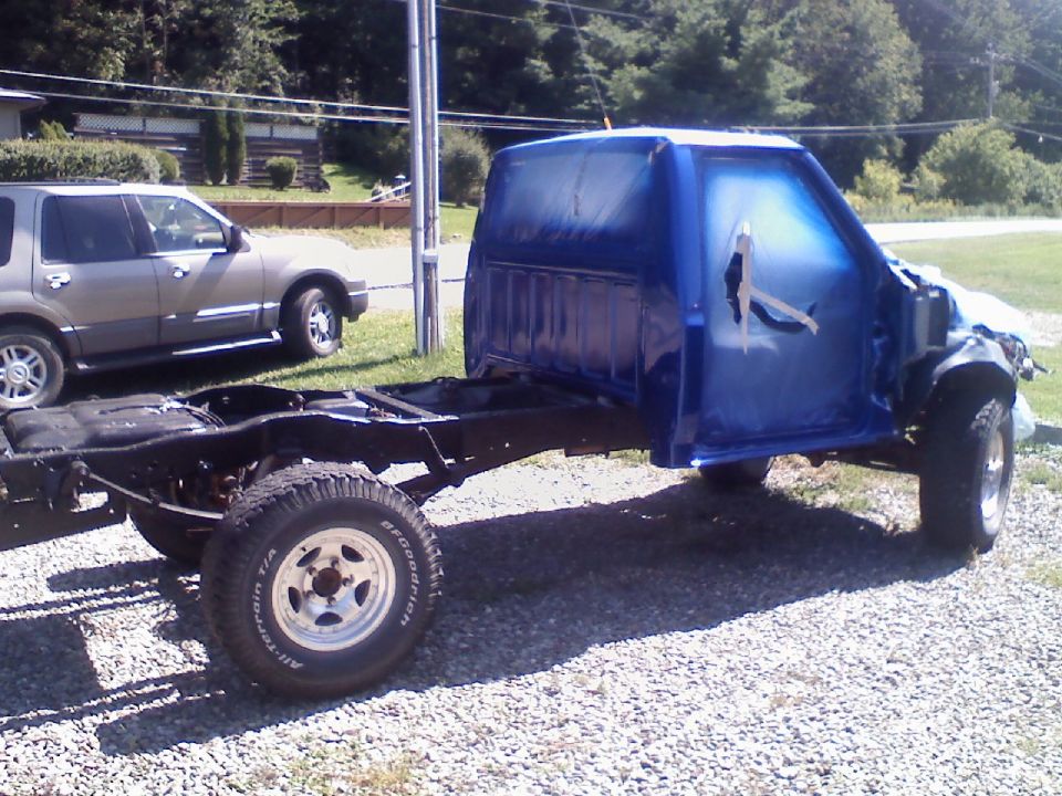 Blue pickup truck cab and chassis being painted, with another SUV parked nearby