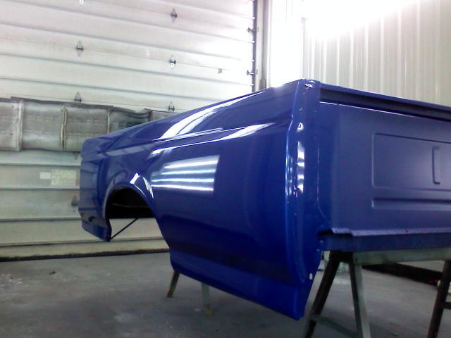 Blue pickup truck bed on sawhorses in a garage, freshly painted