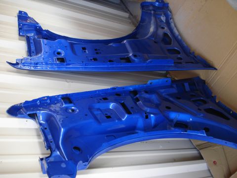 1993 Ford F-150 - Two blue painted vehicle body parts, likely fender wells and structural components, are displayed against a corrugated metal background.