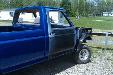 1993 Ford F-150 - This blue pickup truck is missing its front end and has primer on the driver's door.
