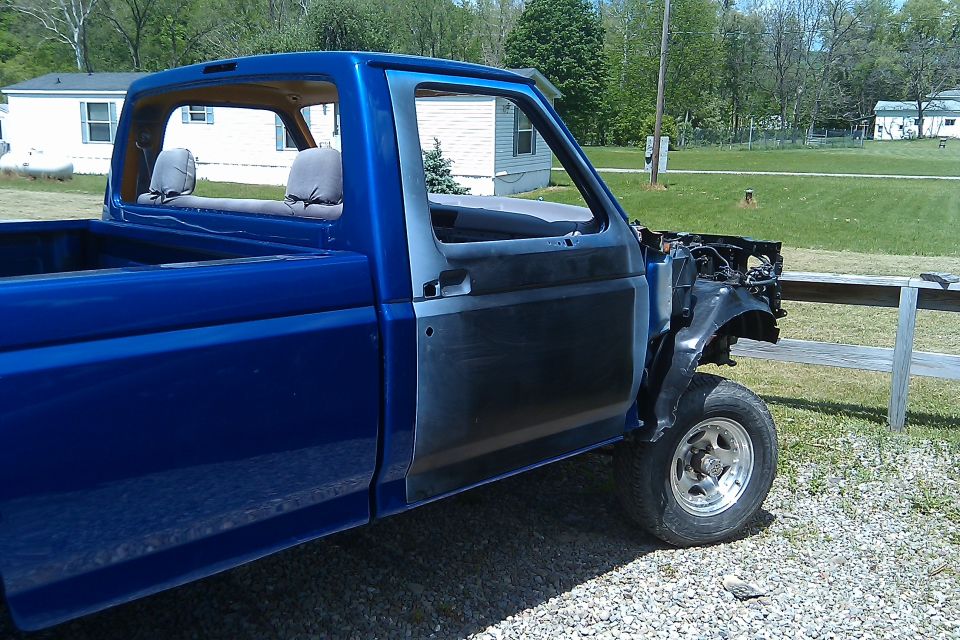 Blue pickup truck with front end removed, showing primer on the driver's door