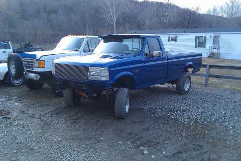 1993 Ford F-150 - A lifted blue Ford F-150 pickup truck is parked next to another truck in front of a mobile home.