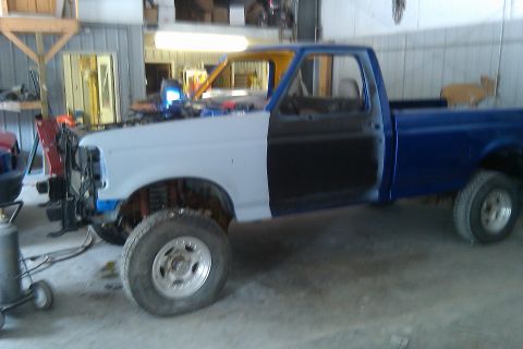 1993 Ford F-150 - Ford F-150 pickup truck in a garage, undergoing bodywork with primer on the front section and blue paint on the rear.