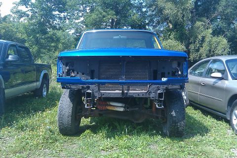 1993 Ford F-150 - Front view of a blue 1992 Ford F-150 truck with its grille and headlights removed, parked next to other vehicles.
