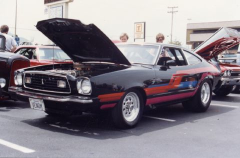 1981 Ford Bronco - A black Ford Mustang II with custom graphics and its hood open is displayed at an outdoor event.