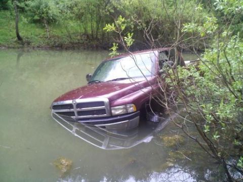 1993 Ford F-150 - A maroon pickup truck is partially submerged in murky water, with its front end facing the camera.