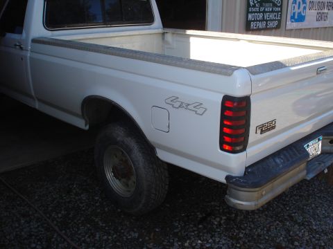 1993 Ford F-150 - A white pickup truck is parked in front of a repair shop. The truck has a diamond plate bed rail protector.