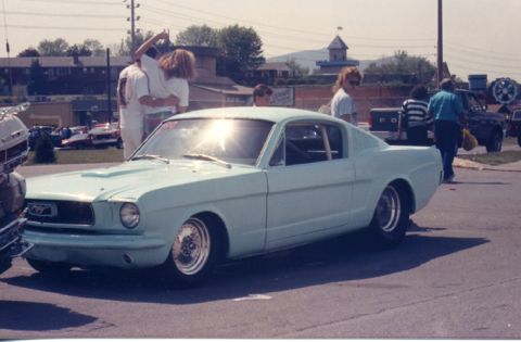 1981 Ford Bronco - A light blue 1965 Ford Mustang coupe is seen from a three-quarter front view, a racing roll cage and custom wheels.