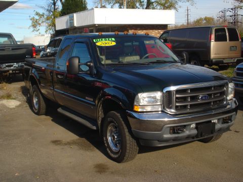 1993 Ford F-150 - A dark green Ford F-Series truck is parked outside a building with other vehicles visible.
