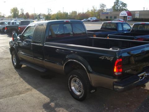 1993 Ford F-150 - A dark green and tan Ford F-250 Super Duty pickup truck is parked in a lot with other vehicles visible.
