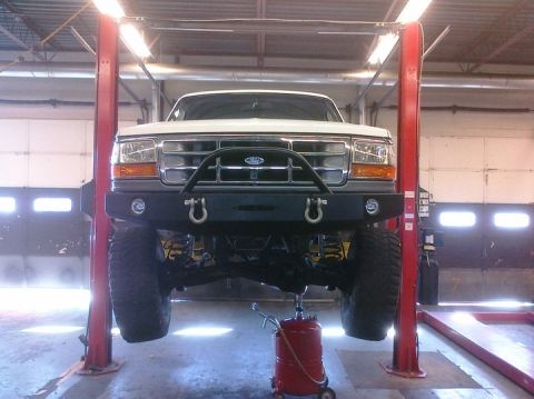 1995 Ford Bronco - Front view of a white 1995 Ford Bronco lifted for service, an aftermarket bumper and visible suspension components.