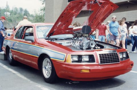 1981 Ford Bronco - Customized red car with a prominent supercharger, hood open, at an outdoor event.