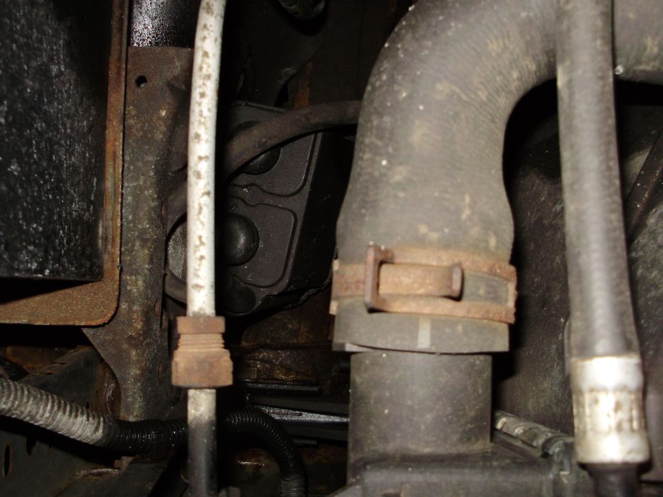 Engine bay hoses and metal brackets with rust. A white pipe is visible on the left