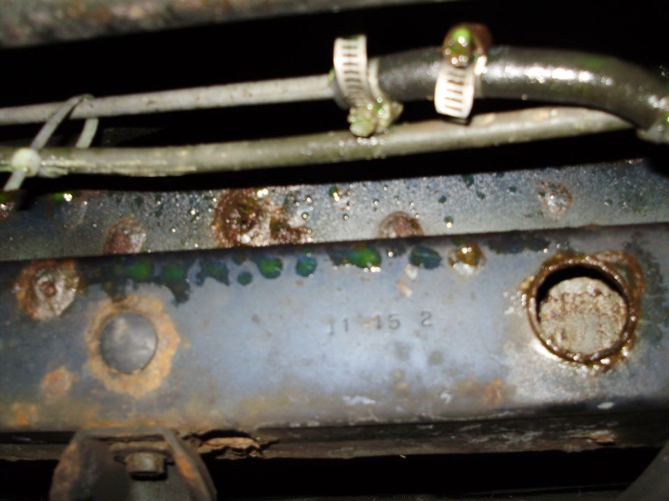 Close-up of rusty vehicle frame with hoses and some green fluid. Numbers '11 15 2' are visible on the frame