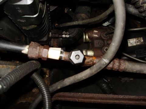 1995 Ford Bronco - A close-up view of a rusty fuel line fitting within an engine bay.