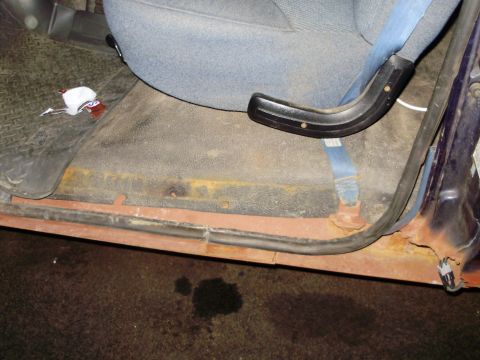 1995 Ford Bronco - The interior door sill shows significant rust, and a blue seatbelt is visible near the grey seat.