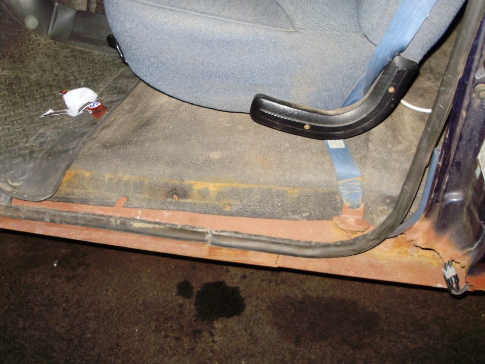 Interior door sill with rust and a blue seatbelt attached to a grey seat