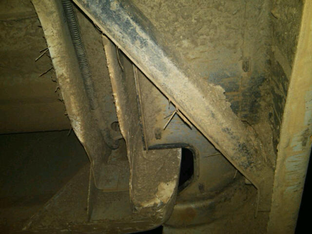 Underside of a dirty vehicle frame with visible rust and a wire conduit