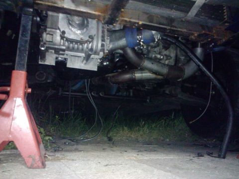 1995 Ford Probe - The vehicle's undercarriage is visible, supported by jack stands, with various engine and exhaust parts exposed.