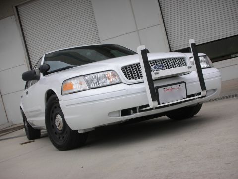 2004 Ford Crown Victoria - A white 2004 Ford Crown Victoria police car is parked in front of a closed garage door, equipped with a push bar.