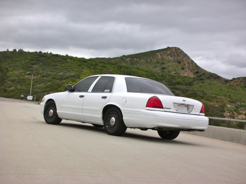2004 Ford Crown Victoria - Rear 3/4 view of a white 2004 Ford Crown Victoria parked on a road with a hilly, green landscape in the background.