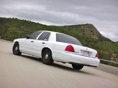 2004 Ford Crown Victoria - Rear view of a white 2004 Ford Crown Victoria parked on a road with a hill in the background.